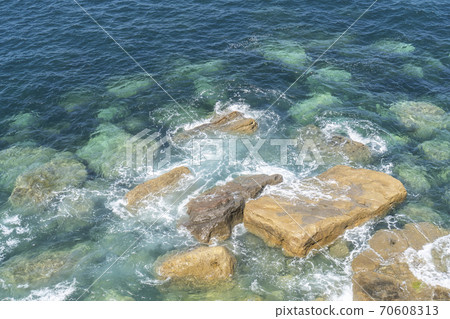 Ocean coast. Clear water. Calm waves crash against stones on a quiet sunny day. Ocean coast. Clear water. Calm waves crash against stones on a quiet sunny day. 70608313