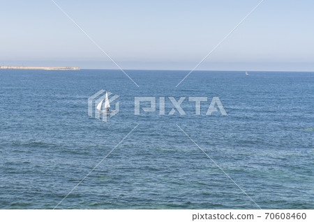 A lonely sailboat sails on the blue calm sea on a sunny summer day. The concept of travel and appeasement A lonely sailboat sails on the blue calm sea on a sunny summer day. The concept of travel and appeasement 70608460