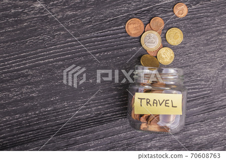 Tilted glass jar with scattered euro coins with the inscription TRAVEL on a black wooden table. The concept of savings for trips to countries and cities. Background for design and lettering, 70608763