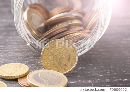 Euro coins in transparent beacon on a black wooden table. Scattered. 70609022