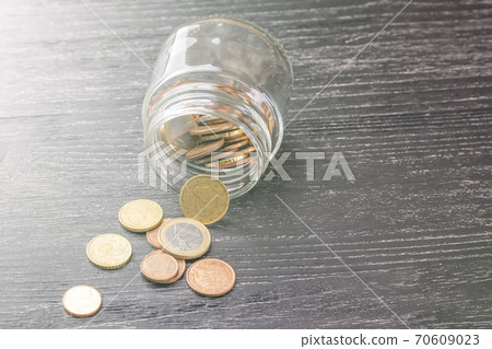 Euro coins in transparent beacon on a black wooden table. Scattered. 70609023