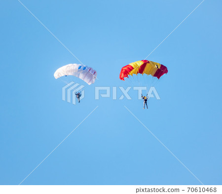 Two parachutists with white parachute floats slowly at low altitude on the background of clear sky Two parachutists with white parachute floats slowly at low altitude on the background of clear sky 70610468