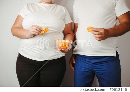 Overweight couple eating unhealthy potato chips 70612146