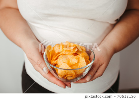 Overweight woman eating fattening potato chips 70612156