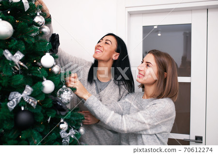 Two young women decorate the Christmas tree, preparing for the New Year's celebration 70612274