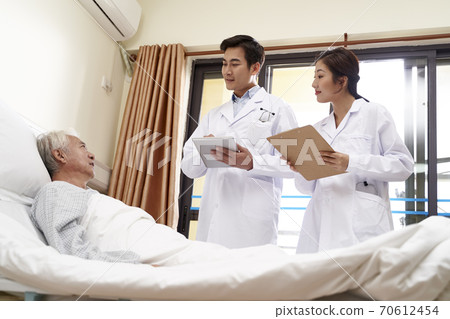 two young friendly asian doctors talking to senior asian male patient at bedside in hospital 70612454