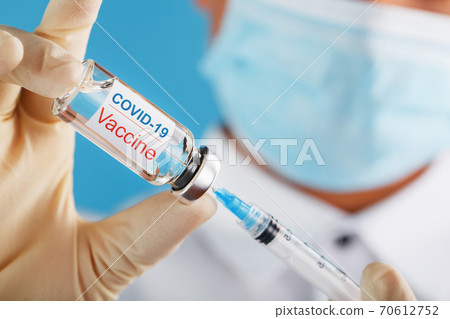 A doctor in rubber gloves takes medicine with a vaccine from an ampoule with a syringe with the text COVID -19 on the ampoule sticker. 70612752