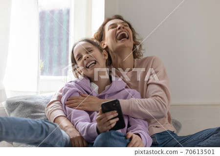 Overjoyed mother and teen daughter laugh using smartphone Overjoyed mother and teen daughter laugh using smartphone 70613501