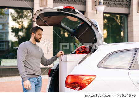 Delivery man standing near car, large festive white box with beautiful red bow at truck. 70614670