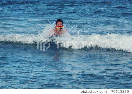 Caucasian man eating piece of watermelon in the sea water Selective focus 70615259