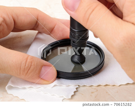 Hands polish a camera polarizing filter using lens pen soft felt end over microfiber cloth.  70615282