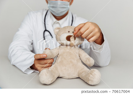 Kind pediatrician in mask treats teddy bear. Child healtcare and treatment concept Kind pediatrician in mask treats teddy bear. Child healtcare and treatment concept 70617004