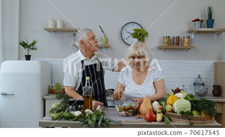 Senior grandparents in kitchen. Funny grandpa joking on grandma. Putting a lettuce about her head Senior grandparents in kitchen. Funny grandpa joking on grandma. Putting a lettuce about her head 70617545