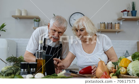 Vegan senior couple cooking salad with raw vegetables. Looking on digital tablet for online recipe 70617575