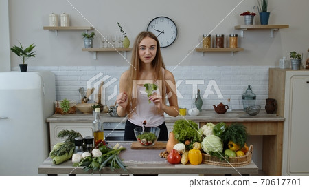 Young girl dancing, having fun and cooking salad with raw vegetables. Throwing pieces of lettuce Young girl dancing, having fun and cooking salad with raw vegetables. Throwing pieces of lettuce 70617701