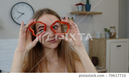 Joyful young girl vegan dancing holding fresh red slice of bell pepper on eyes. Healthy nutrition Joyful young girl vegan dancing holding fresh red slice of bell pepper on eyes. Healthy nutrition 70617710