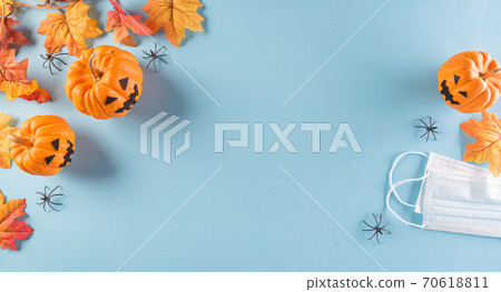 Halloween decorations made from pumpkin, paper bats and surgical face mask on pastel blue background. Flat lay, top view of Halloween celebration during covid-19 pandemic situation. 70618811