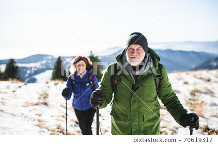 Senior couple with nordic walking poles hiking in snow-covered winter nature. 70619312