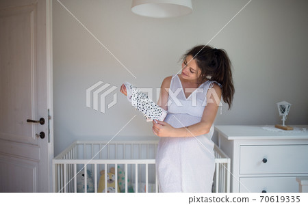 Portrait of pregnant woman indoors at home, holding girls bodysuit. Portrait of pregnant woman indoors at home, holding girls bodysuit. 70619335