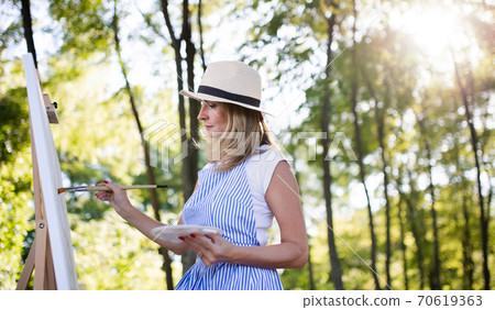 Portrait of mature woman with pallete painting outdoors in garden. Portrait of mature woman with pallete painting outdoors in garden. 70619363