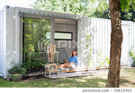 Mature woman working in home office in container house in backyard. Mature woman working in home office in container house in backyard. 70619365