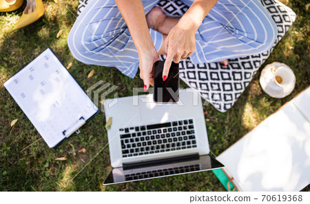 Unrecognizable woman working in home office outdoors in garden, using smartphone and laptop. Unrecognizable woman working in home office outdoors in garden, using smartphone and laptop. 70619368