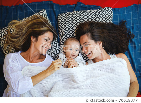 Top view of woman with daughter and baby granddaughter resting on blanket. 70619377