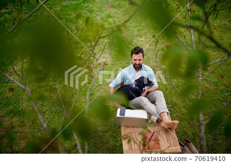 Business man with dog and laptop working outdoors in garden, home office concept. 70619410