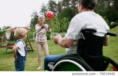 Small boy with senior grandparents in wheelchair playing with a ball in garden. 70619480