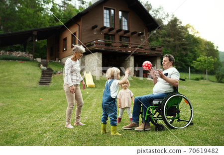 Small children with senior grandparents in wheelchair playing with a ball in garden. Small children with senior grandparents in wheelchair playing with a ball in garden. 70619482