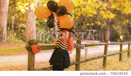 Little girl in the autumn park. A child in a witch costume on Halloween with large colored balloons Little girl in the autumn park. A child in a witch costume on Halloween with large colored balloons 70619545