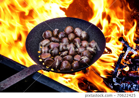 roasting chestnuts in a skillet with holes on the fire 70622425