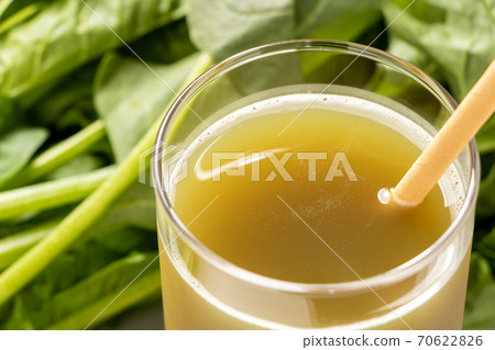 Vegetable juice with a paper straw. Spinach in the back of the photo. 70622826
