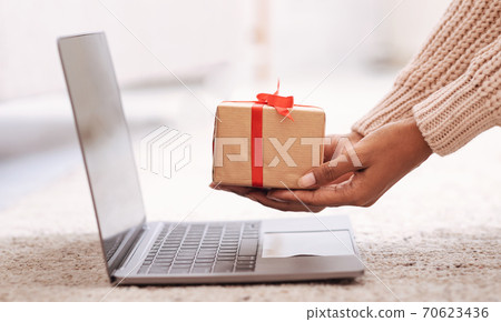 Woman showing gift box to laptop screen Woman showing gift box to laptop screen 70623436