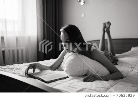 Pensive dreamy female holding book at home looking at big window dreaming, thoughtful young woman 70623929