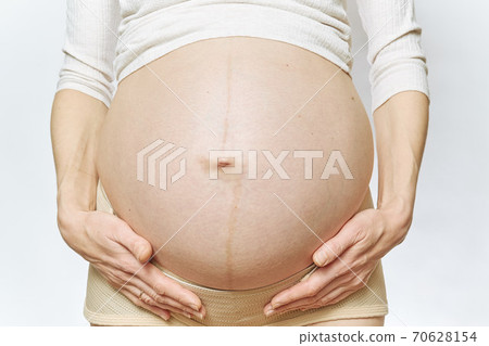 A faceless pregnant woman holds her belly with her hands. close-up 70628154