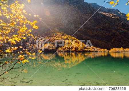 Mountain lake with transparent water and colorful autumnal trees. Mountains and lake Mountain lake with transparent water and colorful autumnal trees. Mountains and lake 70628336