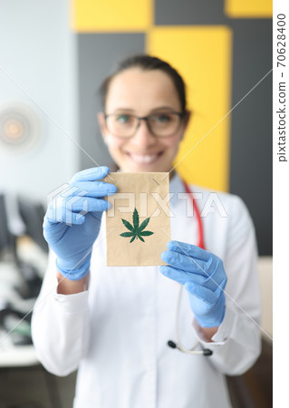 Doctor in white coat holds packet with marijuana sign. Doctor in white coat holds packet with marijuana sign. 70628400