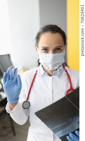 Female doctor in protective medical mask is holding an X-ray. Female doctor in protective medical mask is holding an X-ray. 70628401