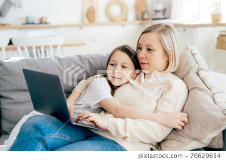 Mom and daughter lie on the couch and hug, look at the laptop screen. Mom and daughter lie on the couch and hug, look at the laptop screen. 70629654