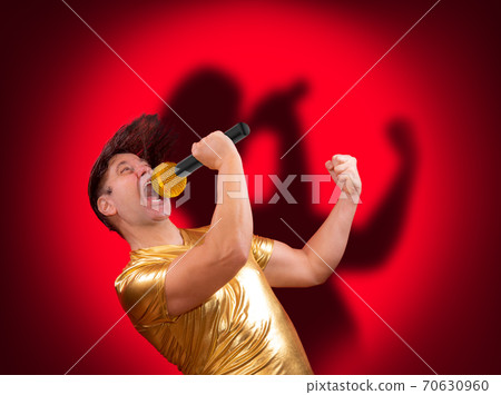 The excited singer with a microphone with own shadow on red background. The excited singer with a microphone with own shadow on red background. 70630960