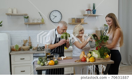 Elderly couple in kitchen receiving vegetables from grandchild. Raw food healthy eating diet Elderly couple in kitchen receiving vegetables from grandchild. Raw food healthy eating diet 70631887