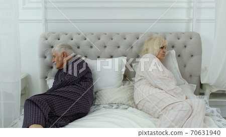 Senior elderly couple in pyjamas lying on bed having an argument in bedroom. Grandparents quarrel 70631940
