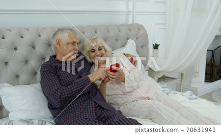 Senior elderly couple wearing pyjamas lying on bed looking on mobile phone laughing and having fun 70631941