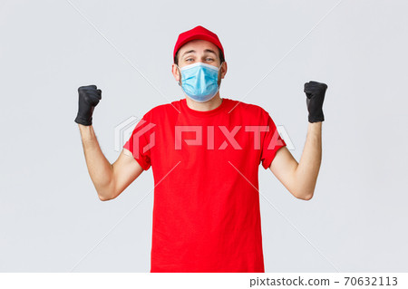 Covid-19, self-quarantine, online shopping and shipping concept. Excited delivery man feel rejoice and happiness, fist pump in celebration, success, achieve goal, wear medical mask and uniform cap 70632113