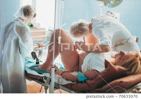 In the Hospital Midwife Gives Newborn Baby to a Mother to Hold, Supportive Father Sitting Near Wife. Happy Family in the Modern Delivery Ward. 70633070
