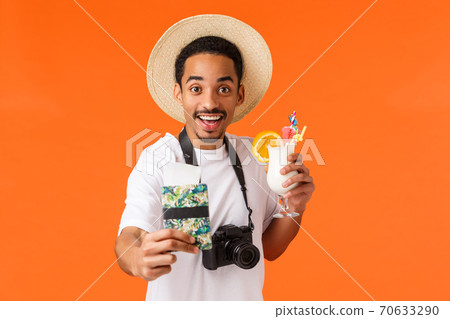 Fly with me. Cheerful outgoing smiling, happy african-american man stretching hand towards camera and giving you passport with tickets, holding cocktail and smiling, inviting to vacation 70633290