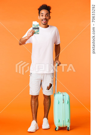 Full-length vertical shot happy upbeat, african american man with luggage, holding passport with two flight tickets, smiling amused, flying abroad, travel on vacation, standing orange background Full-length vertical shot happy upbeat, african american man with luggage, holding passport with two flight tickets, smiling amused, flying abroad, travel on vacation, standing orange background 70633292