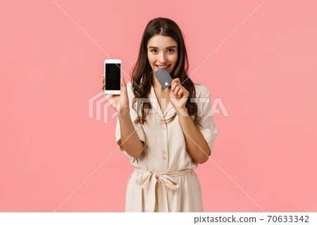 Romance, love and shopping concept. Cheerful carefree young woman order online, holding smartphone, biting credit card and smiling tempting, want buy new clothes, promote application, pink background 70633342