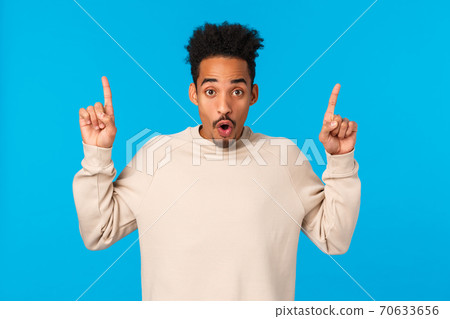 Have you seen it. Attractive impressed african-american guy with moustache, afro haircut, saying wow, telling about event, product advertising, pointing fingers up over blue background 70633656